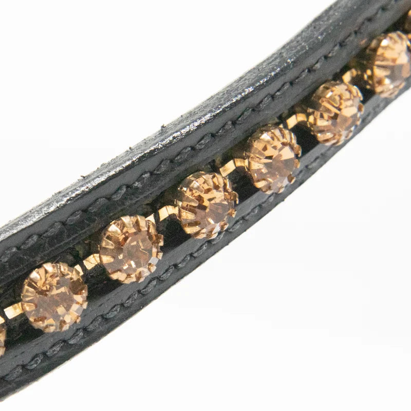Close-up of a black leather browband featuring a row of faceted champagne-colored rhinestones set in gold-toned metal, against a plain white background.
