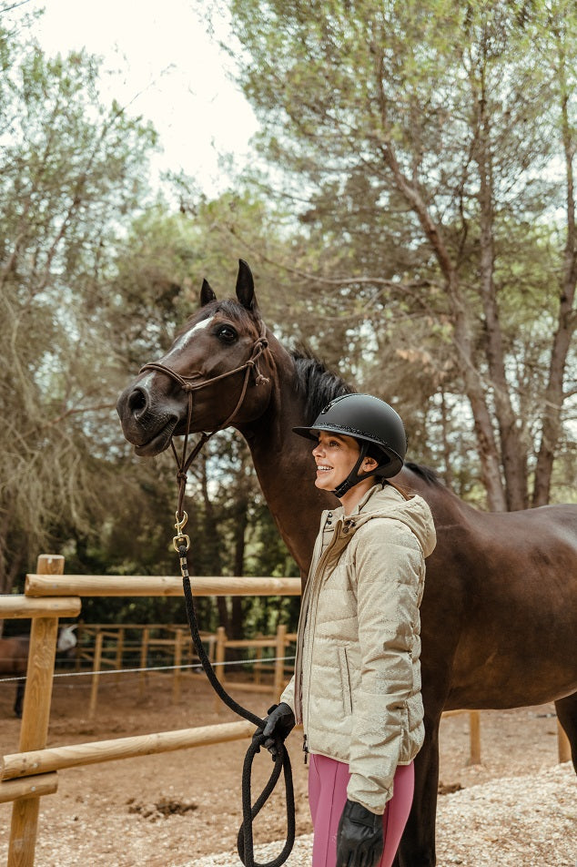 Woman in equestrian gear standing next to a horse in an outdoor setting