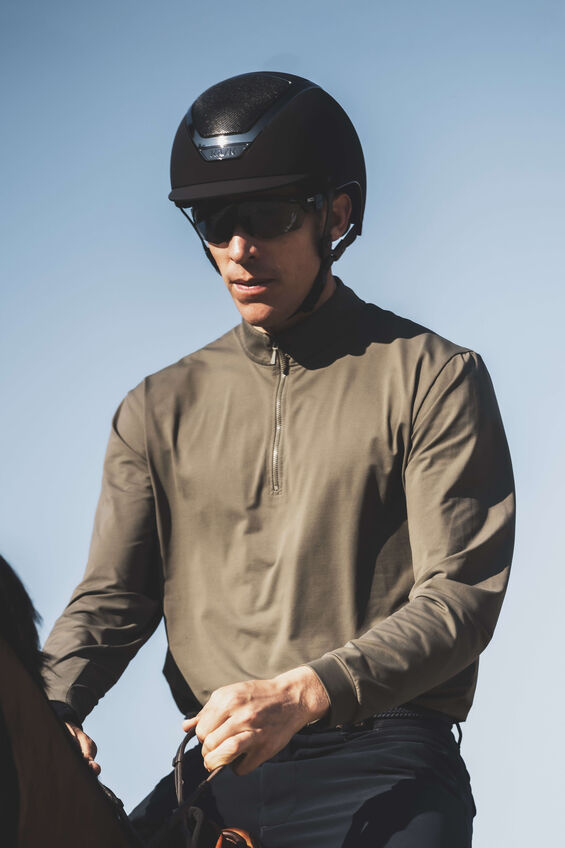 Man on a horse wearing a black helmet with sky behind him