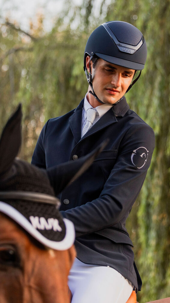 Man in equestrian attire sitting on a horse with trees in the background
