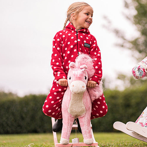 Child in a red polka dot coat holding a pink plush horse outdoors.