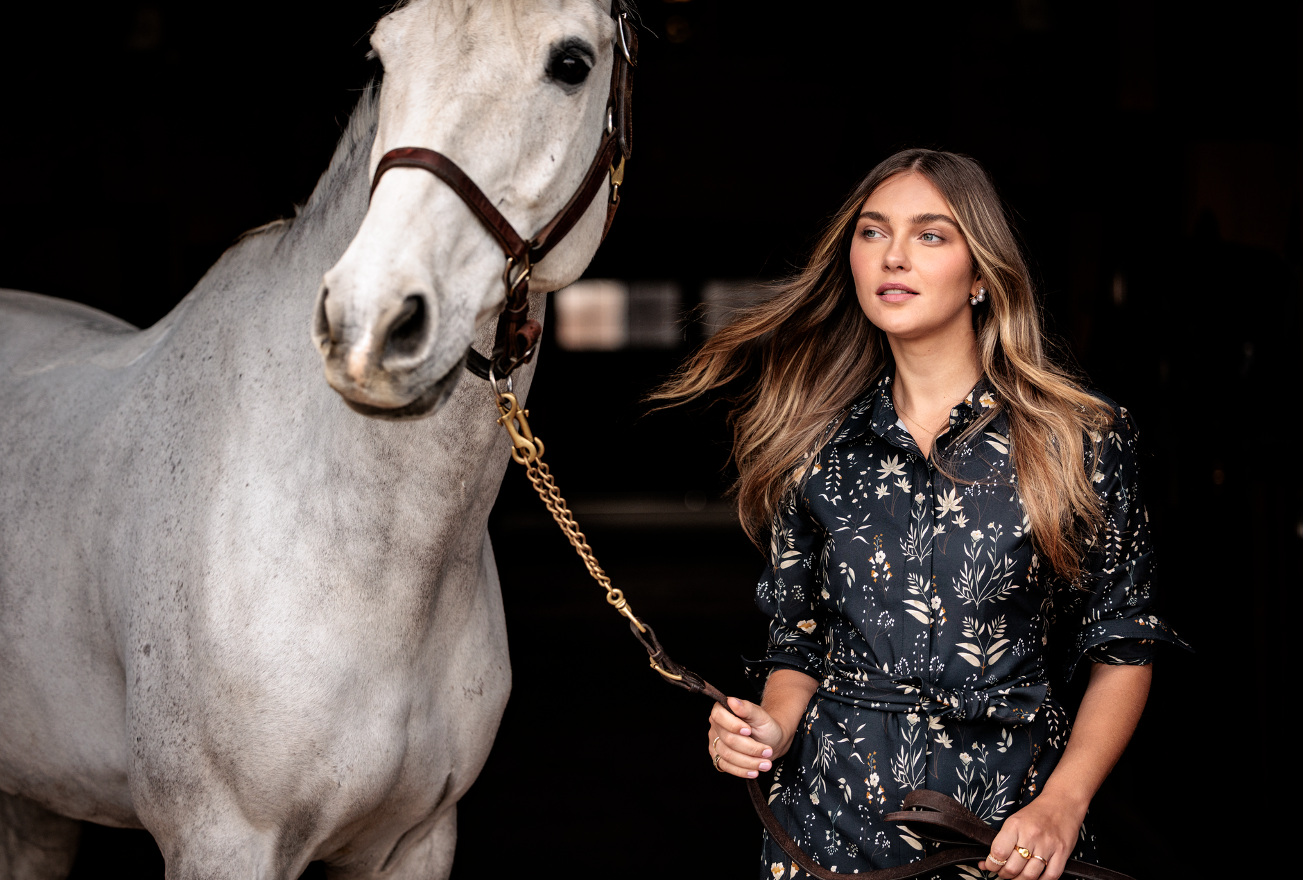 Woman standing next to a white horse in a dark setting