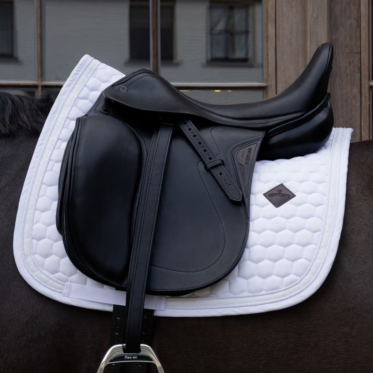 Black saddle on a white quilted saddle pad with a blurred indoor background