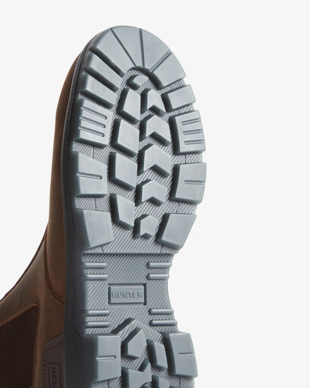 Close-up of a brown leather shoe with a gray sole on a light gray background