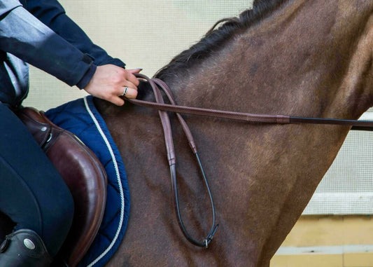 Close-up of a rider's hand holding brown rubber reins on a horse.
