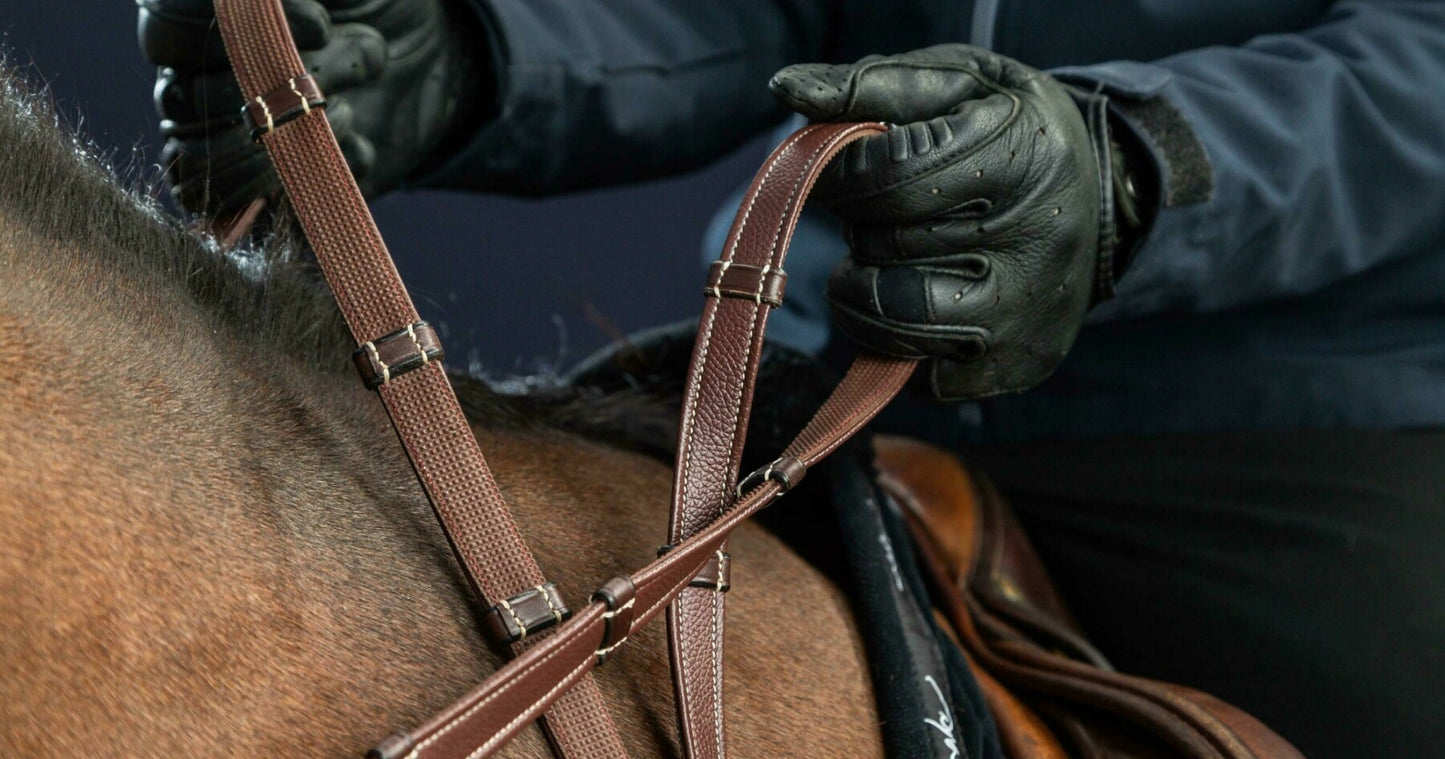 Person adjusting a brown bridle on a horse's head, wearing dark gloves against a dark background.