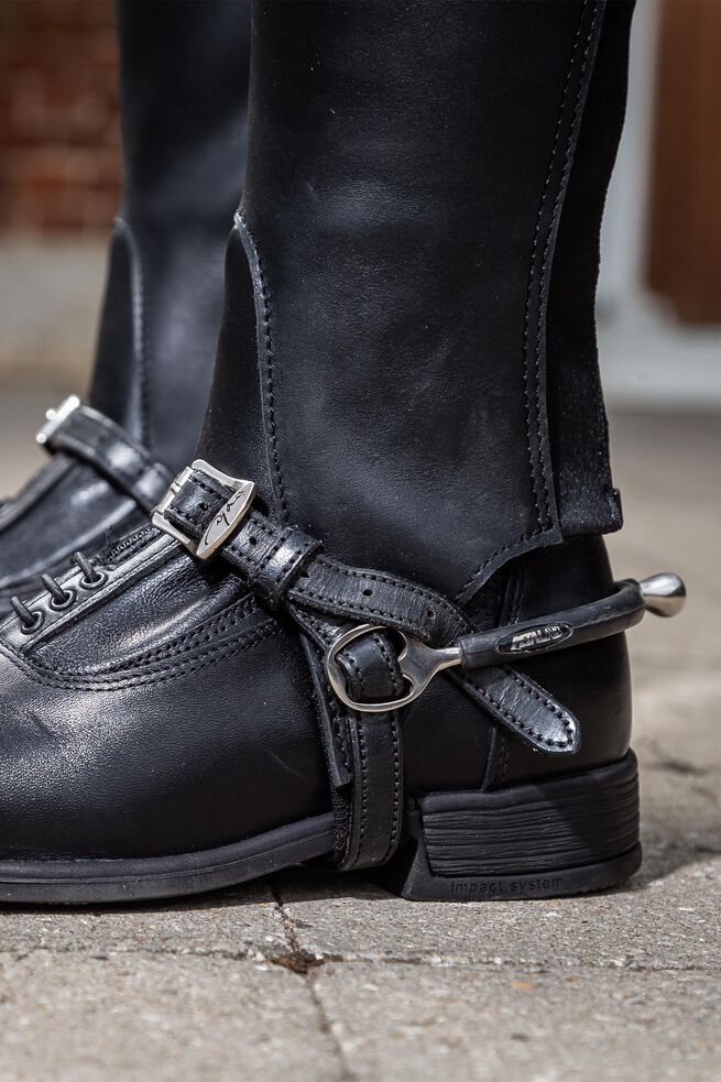Close-up of black leather boots with metal buckles on a concrete surface.