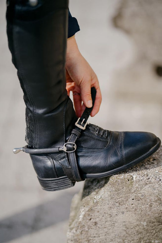 Person adjusting a black leather boot with a strap on a concrete surface
