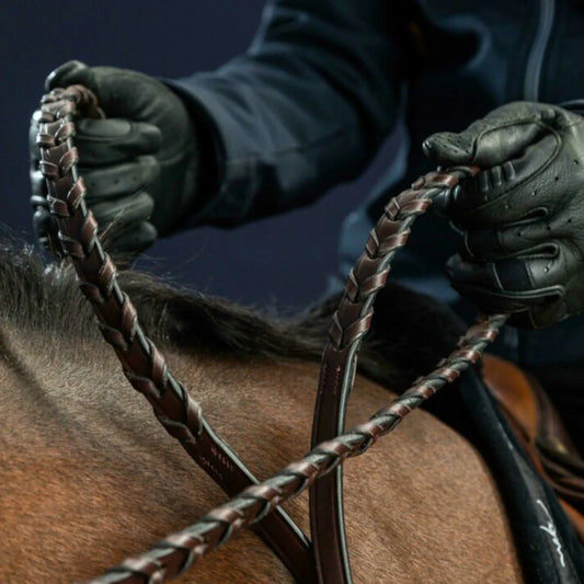 Close-up of gloved hands holding a horse bridle with a dark background