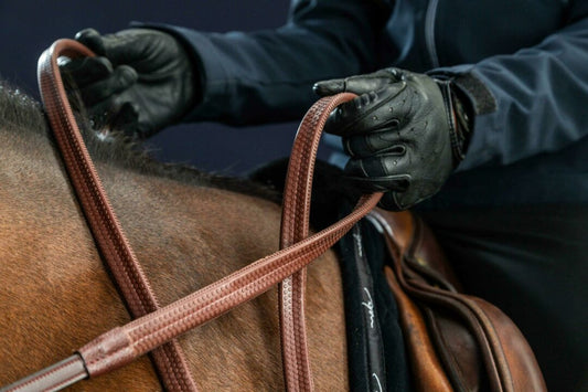 Close-up of a person wearing gloves holding a horse bridle with a dark background