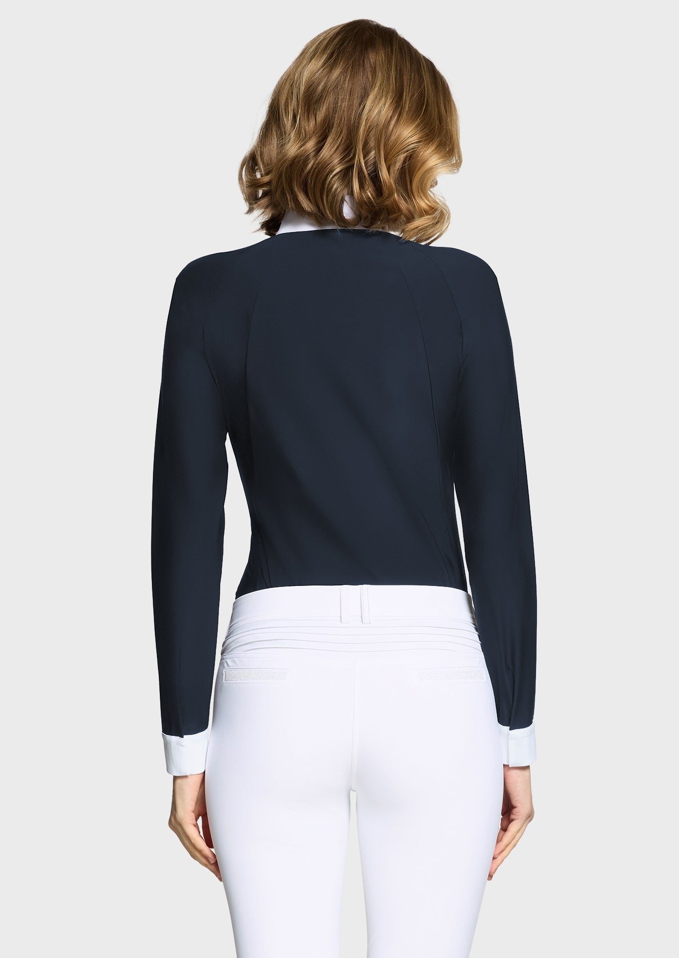 Woman wearing a navy competition shirt and white breeches on a beige background