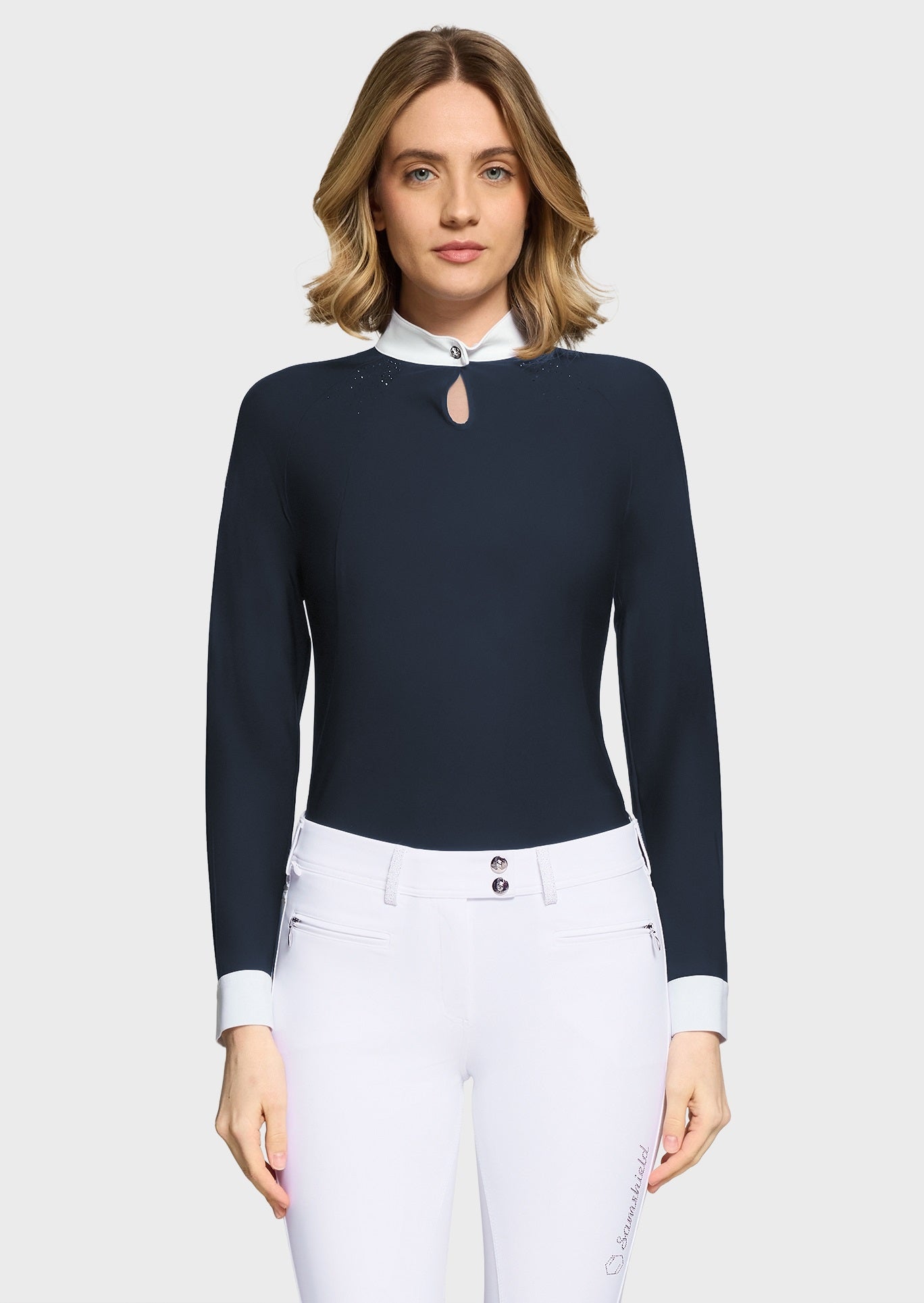 Woman wearing a navy competition shirt and white breeches on a beige background