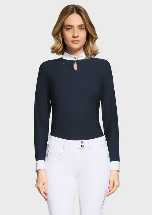 Woman wearing a navy competition shirt and white breeches on a beige background