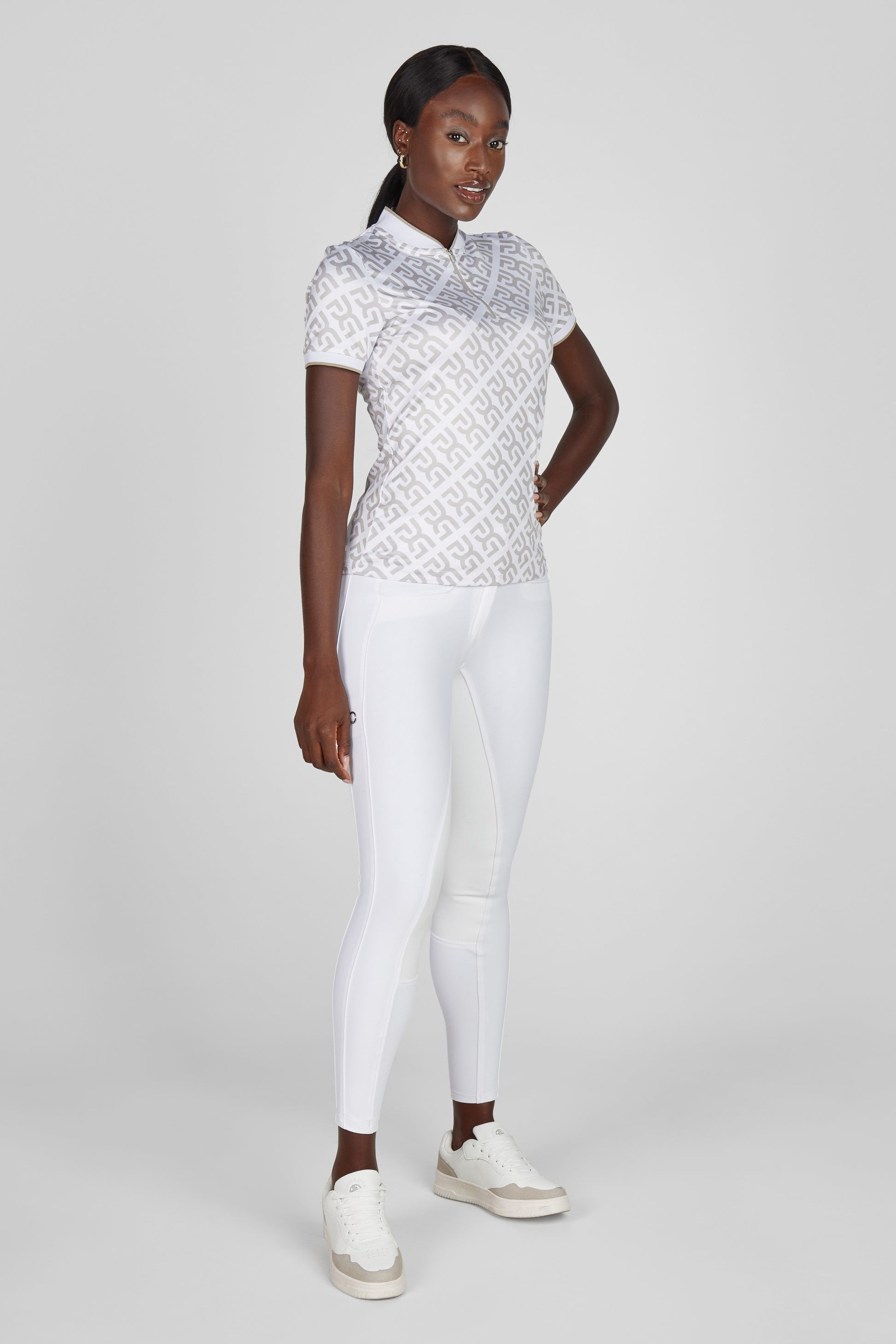 Woman wearing a white patterned top and white leggings on a gray background