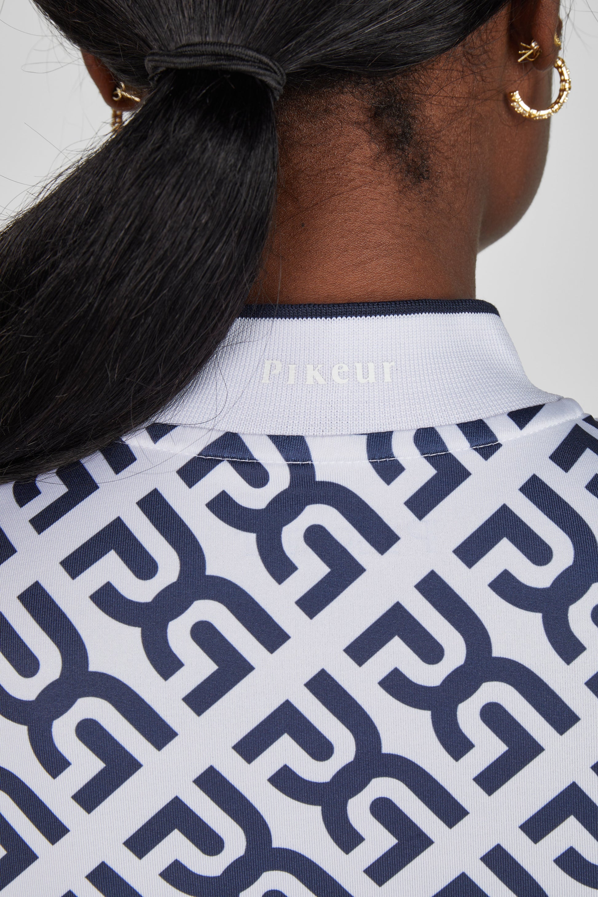 Person wearing a white shirt with a blue geometric pattern, brand 'R' visible.