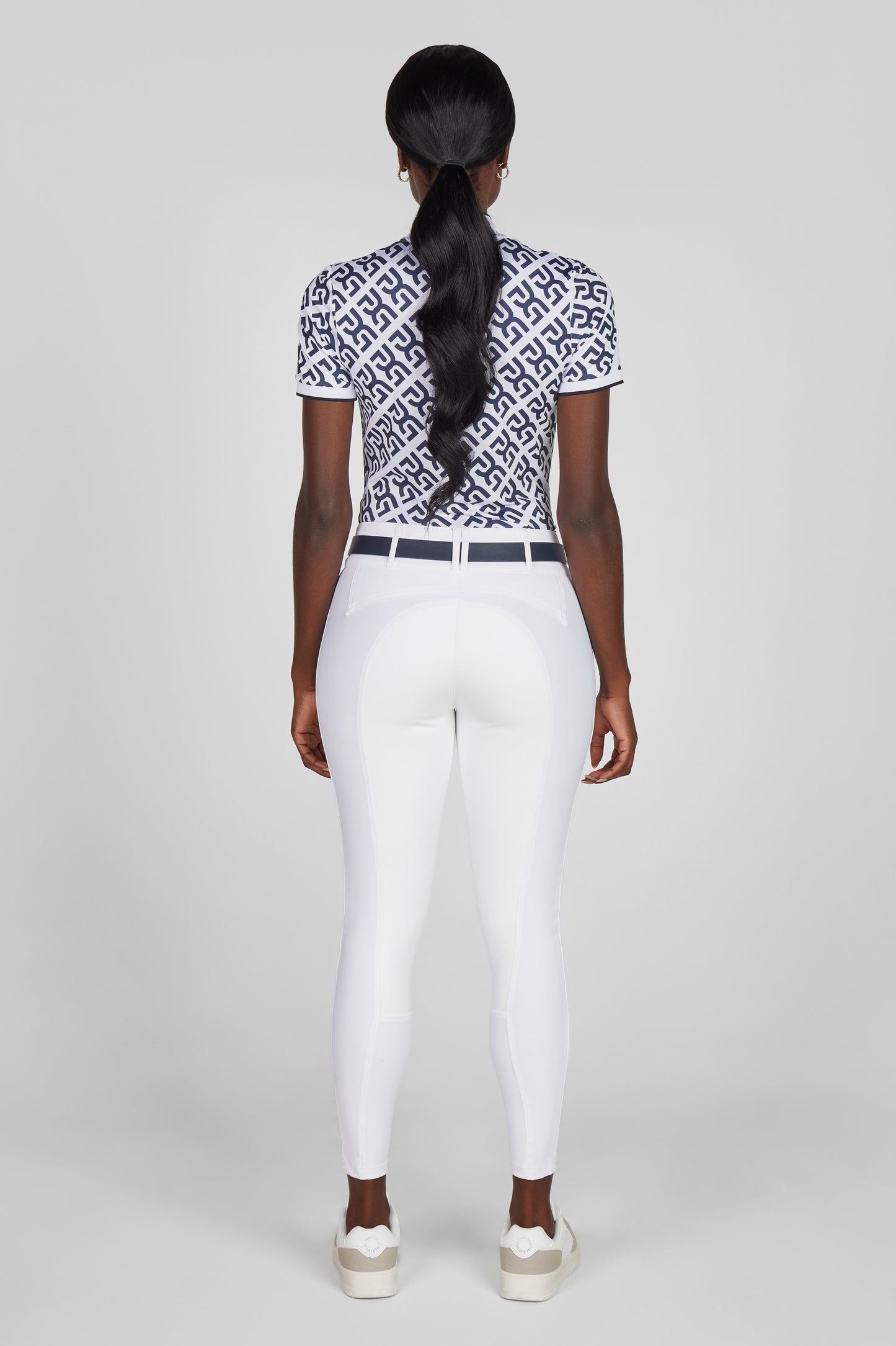 Person wearing a patterned top and white pants on a light gray background