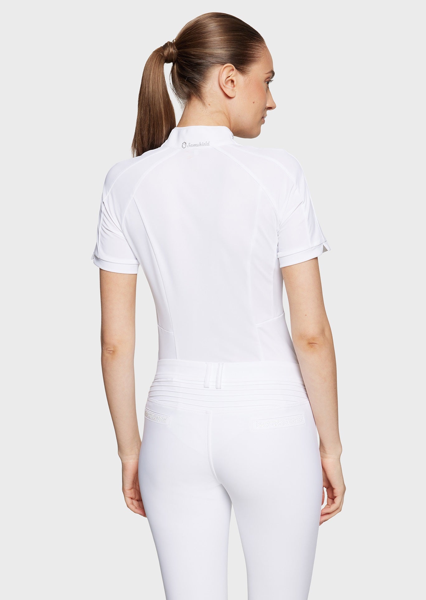 Woman wearing a white competition shirt and white breeches on a beige background