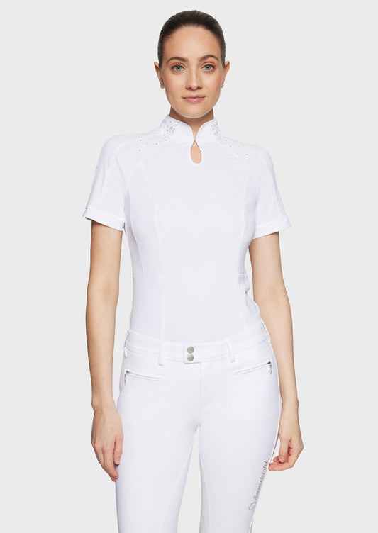 Woman wearing a white competition shirt and white breeches on a beige background