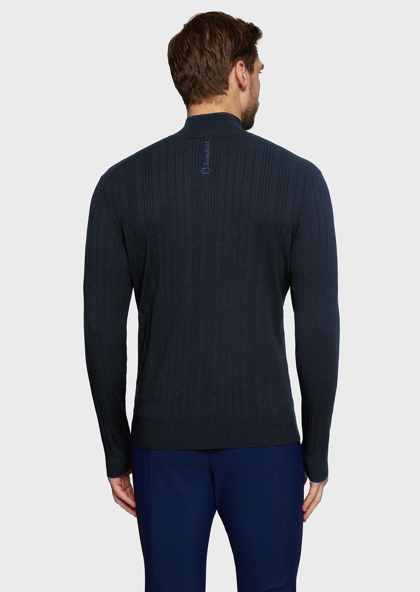 Man wearing a navy knitted jumper and blue breeches on a beige background