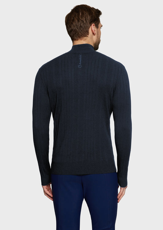 Man wearing a navy knitted jumper and blue breeches on a beige background