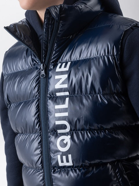 A close-up of a navy blue puffer vest worn by a model, featuring the brand name 'EQUILINE' printed vertically in white on the front.