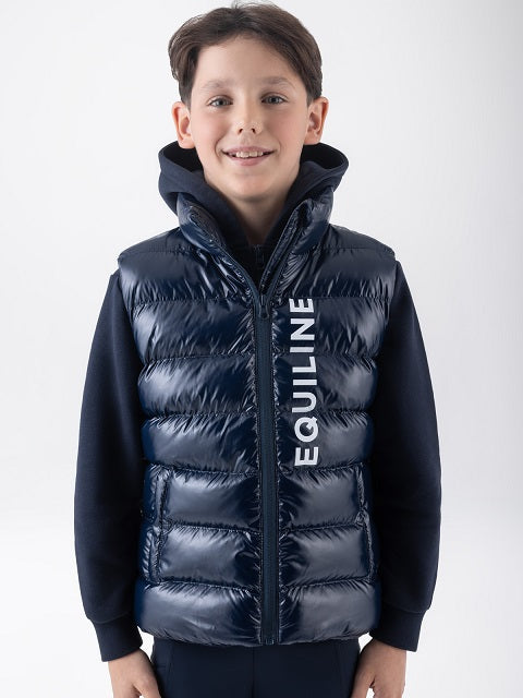 A young boy wearing a navy blue puffer vest over a matching navy hoodie. The vest features a high collar, horizontal quilting, and the brand name 'EQUILINE' printed vertically in white on the front.