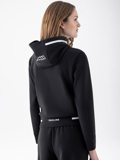 A woman shown from the back wearing a black hooded sweatshirt and matching black pants against a clean white studio background. The hoodie has a white geometric logo on the back of the hood and white text on the waistband.