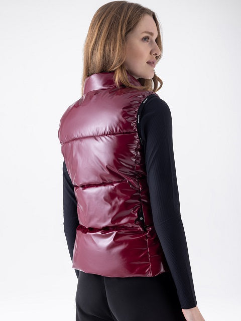 A woman shown from the back wearing a shiny, quilted puffer vest in a deep burgundy or maroon color over a black long-sleeve top, against a plain white studio background.