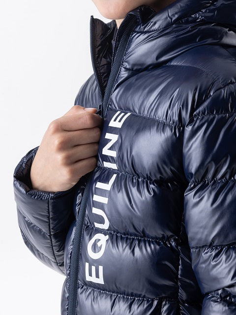 Close-up of a person wearing a shiny navy puffer jacket with large white vertical EQUILINE lettering on the front, holding the zipper closed with one hand against a light gray studio background.