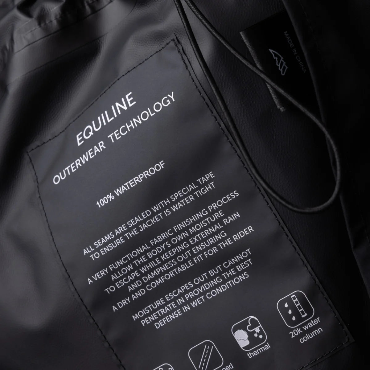 Close-up of a black waterproof jacket interior showing printed white text about 'EQUILINE OUTERWEAR TECHNOLOGY' and a small sewn brand label.