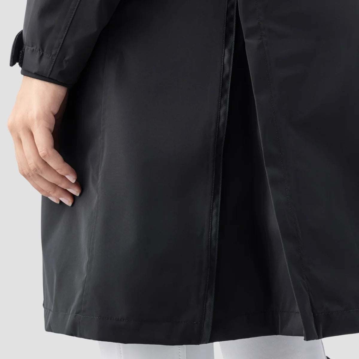 Close-up of a person wearing a black waterproof coat, showing the hand, sleeve, and hem against a light gray background.