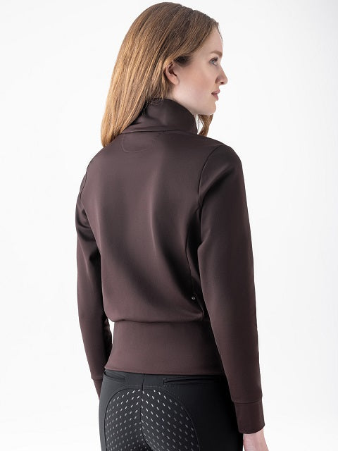 A woman shown from the back wearing a dark brown long-sleeve athletic top and black riding breeches with a textured pattern on the seat, against a plain white studio background.