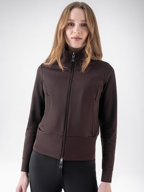 A woman wearing a dark brown full-zip athletic jacket with a mock neck and zippered pockets, paired with black leggings, against a light gray studio background.