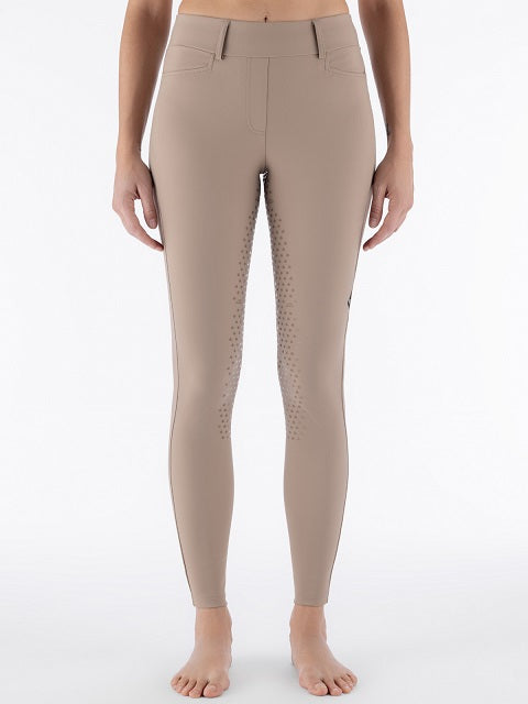 A model wearing high-waisted equestrian riding tights in a solid taupe color, featuring textured grip panels on the inner thighs, shown against a plain white studio background.
