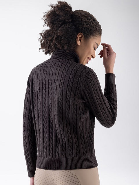 A woman shown from the back wearing a dark brown cable-knit mock-neck sweater and beige patterned pants against a light gray studio background.