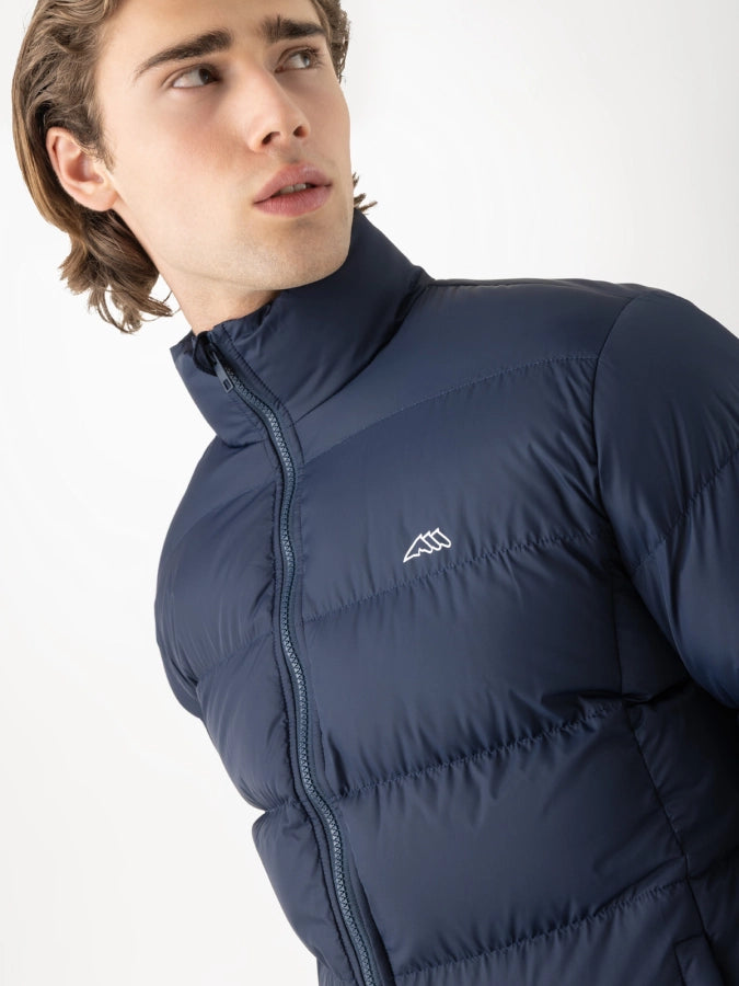 Man wearing a navy padded jacket with the Equiline three horse logo on the chest on a white background