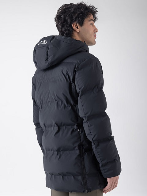 A man wearing a black hooded puffer jacket, shown from a side-back angle against a light gray studio background.