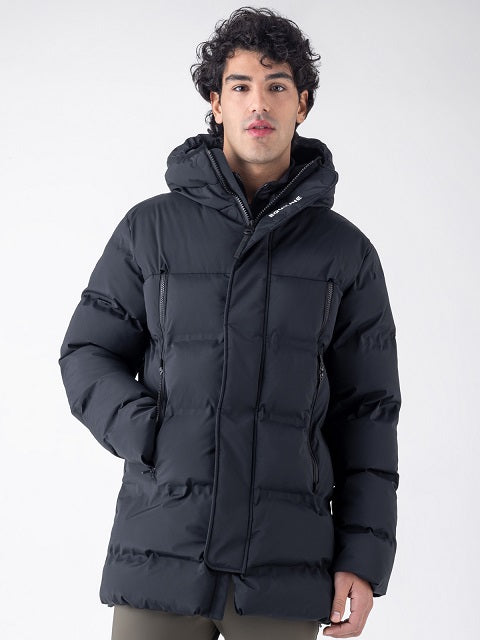 A man wearing a black hooded puffer jacket with horizontal quilting, standing against a light gray studio background.