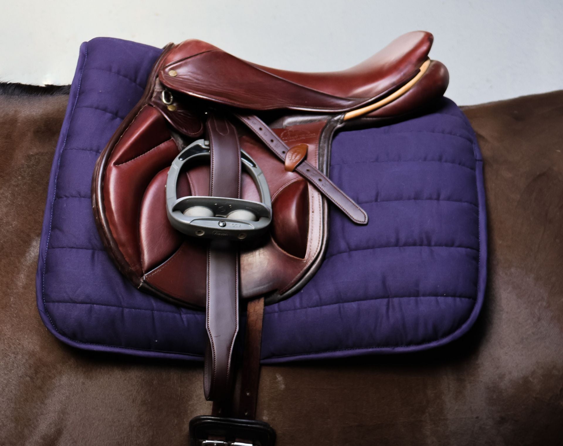 Brown leather saddle on a purple quilted saddle pad on a horse.
