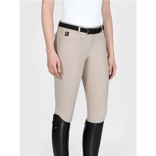 A woman wearing Equiline Ladies Full Grip Breeches in cedar beige, paired with a white riding shirt and black riding boots.