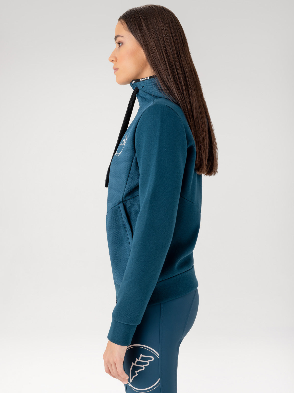 Woman wearing a teal sweatshirt with a logo on a white background