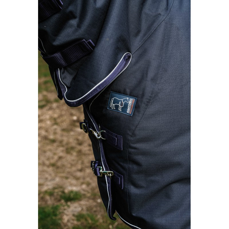 Close-up of a dark blue equestrian saddle pad with a brand logo on a blurred grass background