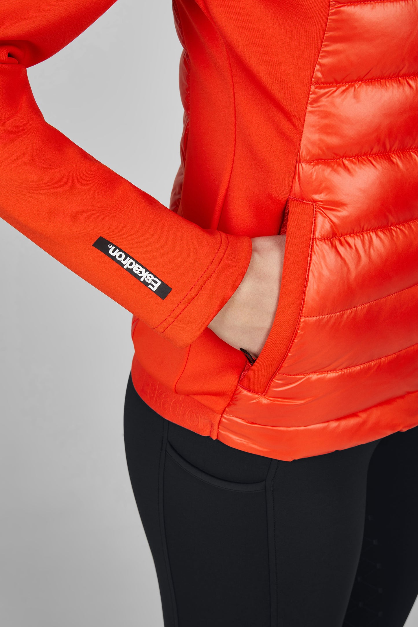 Close-up of a bright orange puffer jacket with a brand logo on a gray background