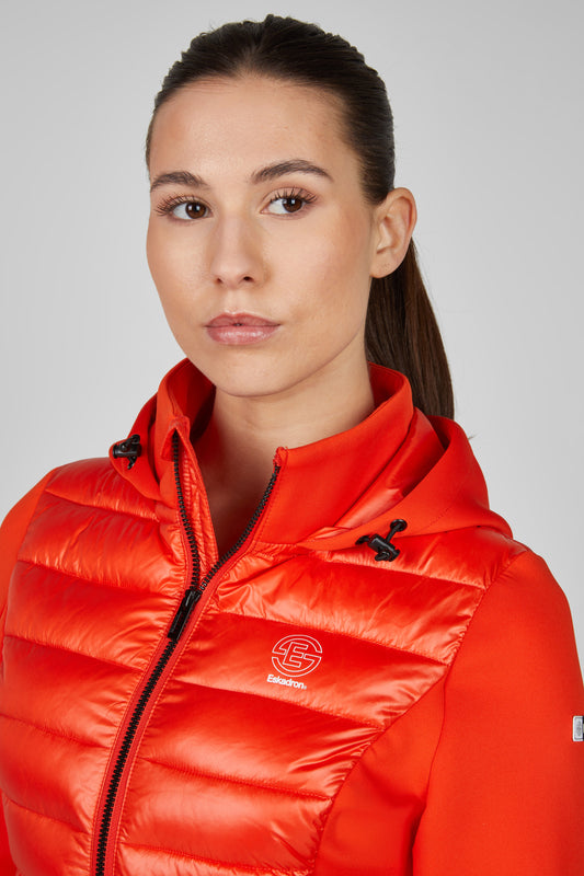 Woman wearing an orange puffer jacket with a brand logo on a gray background