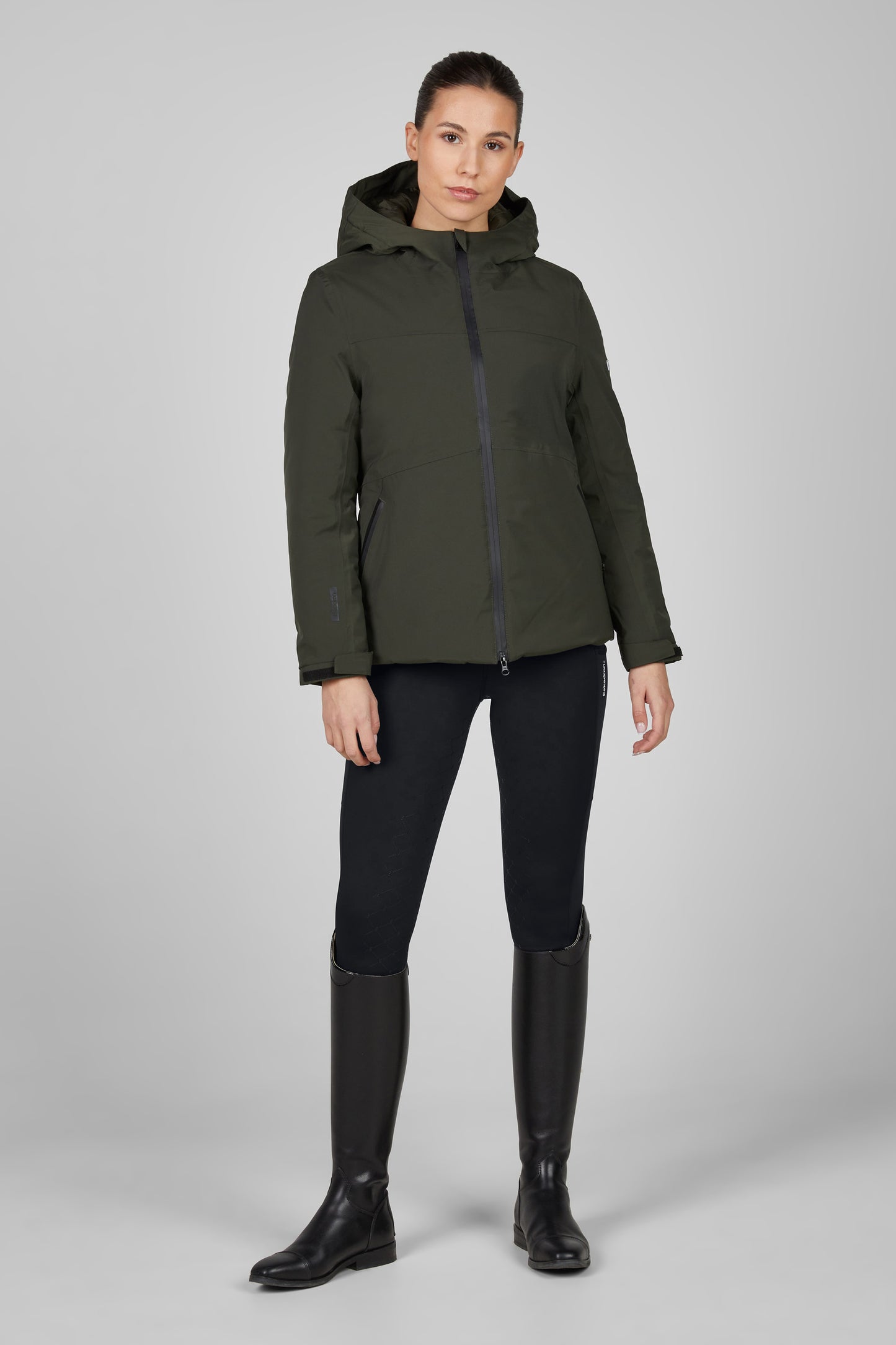 Woman wearing a green jacket and black riding pants on a gray background