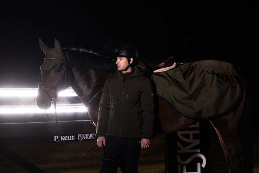Person standing next to a horse in a dark setting with ESKADRON branding.