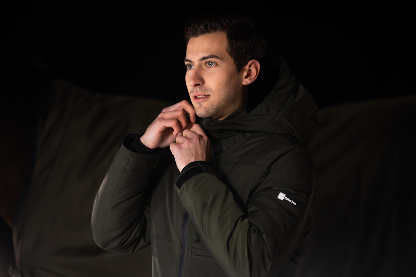 Man wearing a black jacket with a brand logo against a dark background