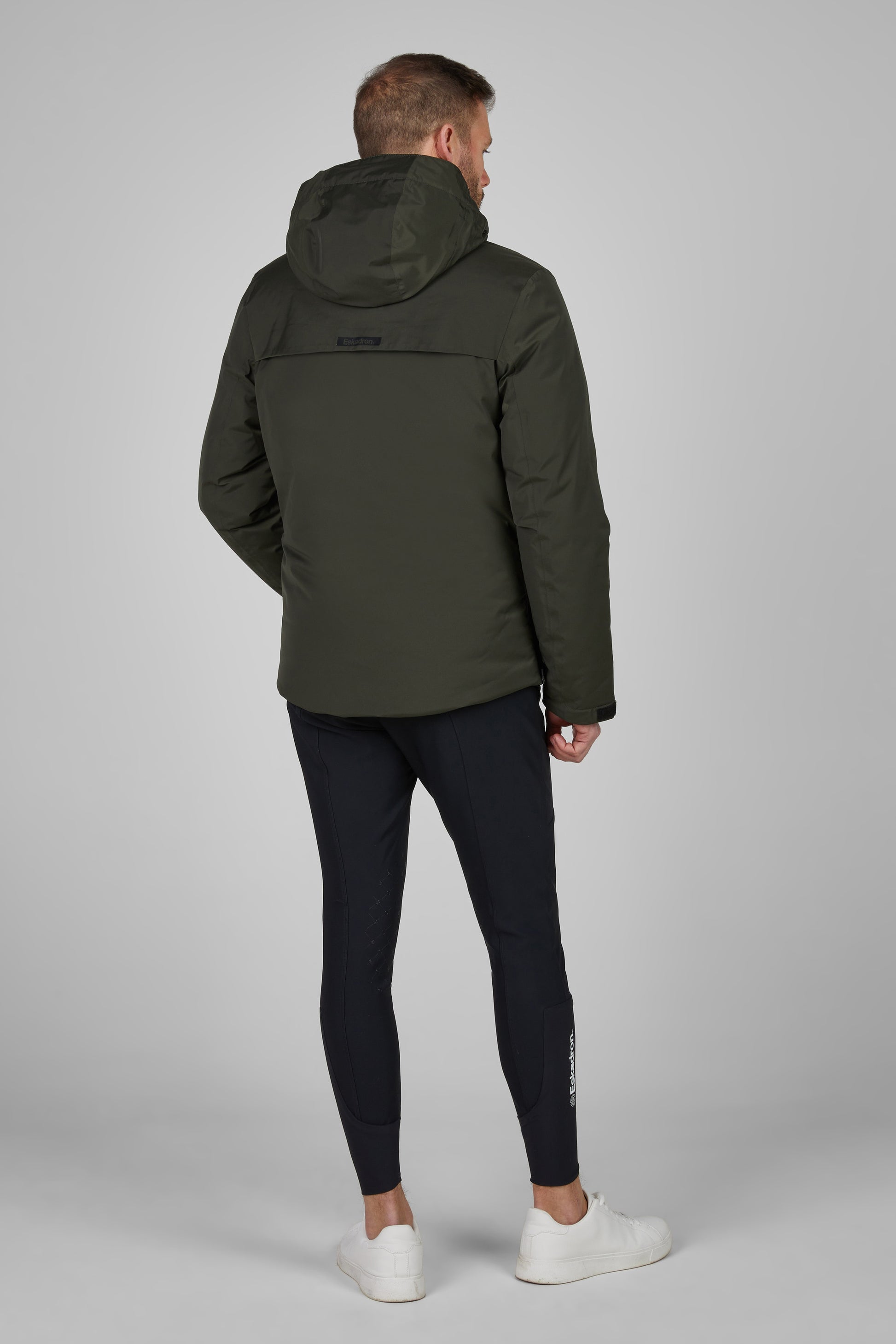 Person wearing a green jacket and black breechess on a gray background