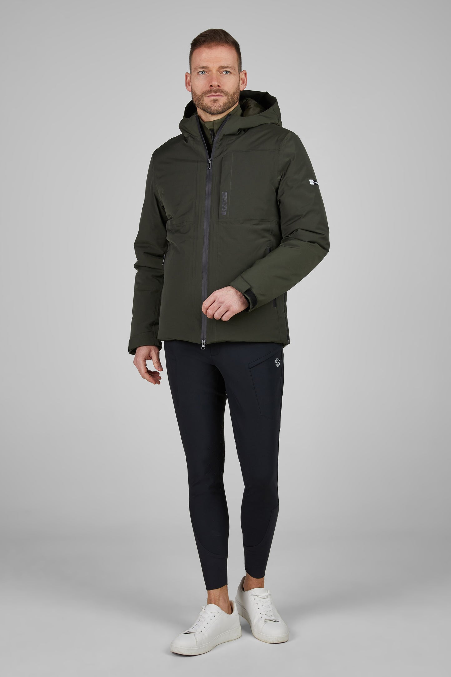 Man wearing a green jacket and black breeches on a gray background