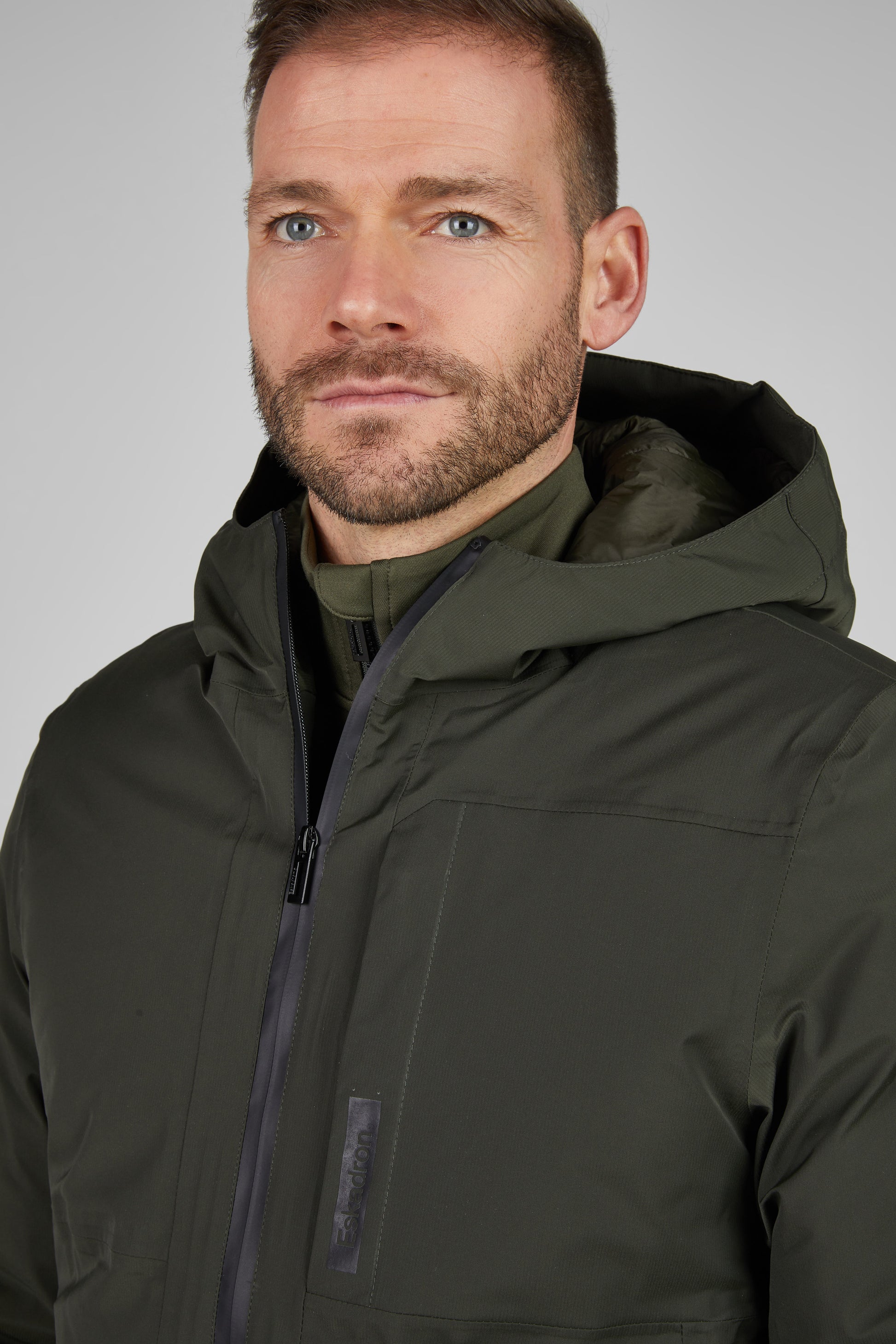 Man wearing a dark green jacket against a plain background